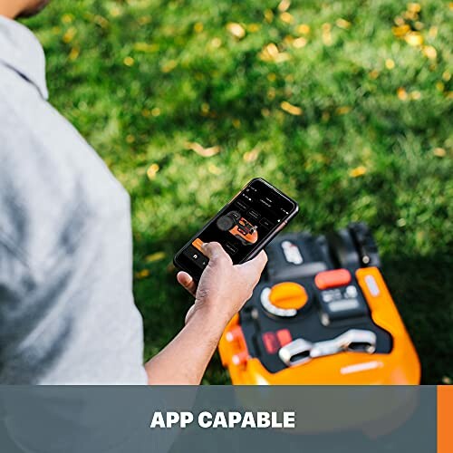 Person using smartphone app to control lawn mower on grass.