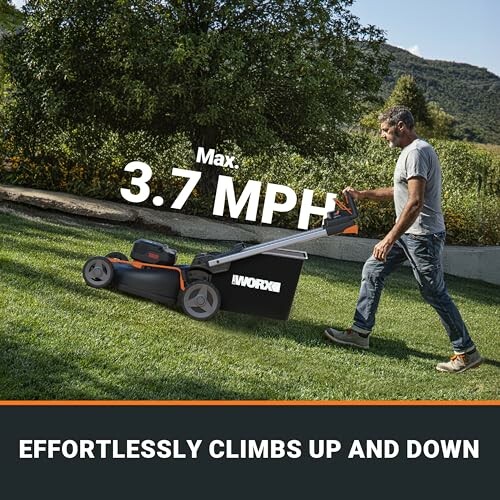 Man using a lawn mower on grass with hills in background.