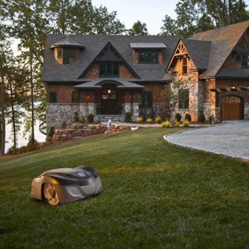 Robotic lawn mower on grass with a modern house in the background.